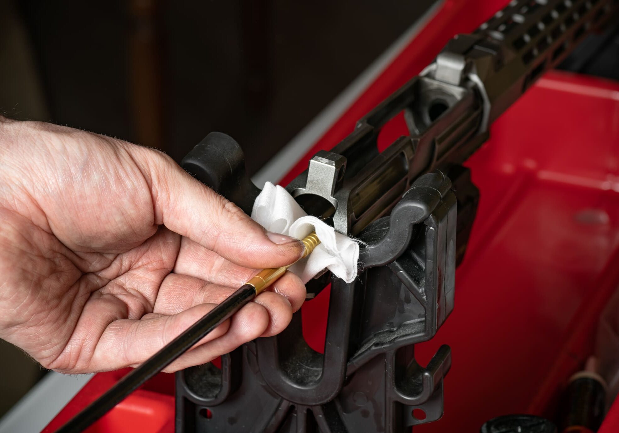 Man`s hand cleaning the gun rifle parts details by special metal cleaning rod red plastic holder background top view